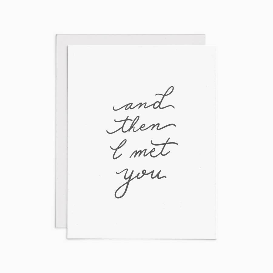 Simple black cursive text reading "And then I met you" on a white card with an off white envelope.